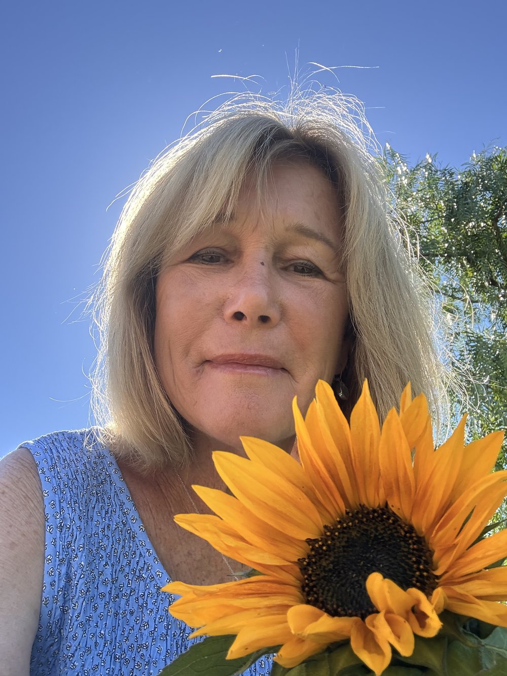Linda, founder of LiNDi Books, smiling beside a sunflower in her garden.